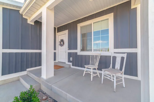 White porch chairs against window and front door of home with gray exterior wall