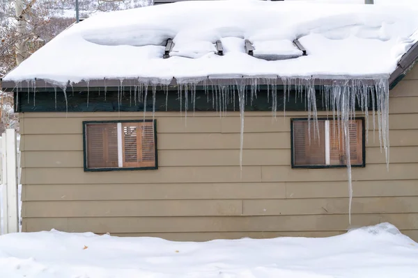 Snow covered roof with row of icicles over windows and wooden wall in Park City