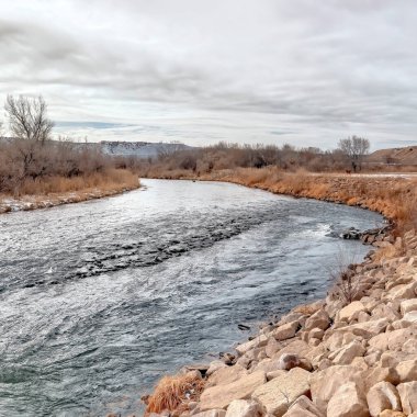 Evler ve tepe manzarası boyunca çimenli ve kayalık kıyıları olan kare ekin nehri.