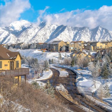 Wasatch tepeleri ve bulutlu mavi gökyüzü manzaralı dağlık evler boyunca kare yol