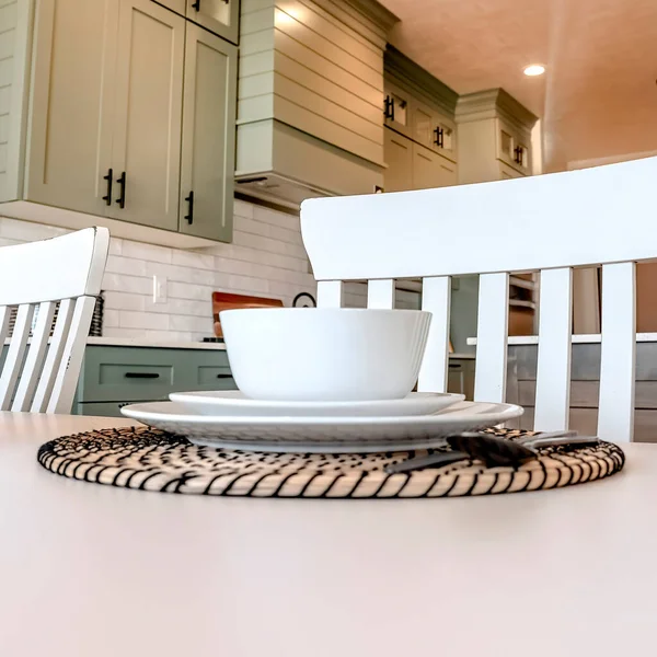 Столовые приборы и посуда на обеденном столе с видом на кухню на заднем плане — стоковое фото