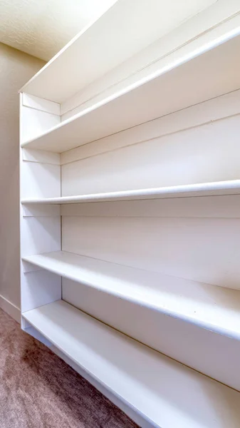Vertical Small walk in closet with empty long cabinet shelves under slanted ceiling — Stock Image Vertical Small walk in closet with empty long cabinet shelves under slanted ceiling Stock Photo