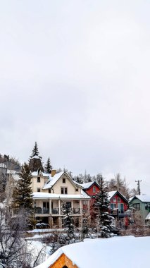 Karla kaplı bir tepenin yamacındaki yerleşim yerinin üzerinde dikey bulutlu bir gökyüzü