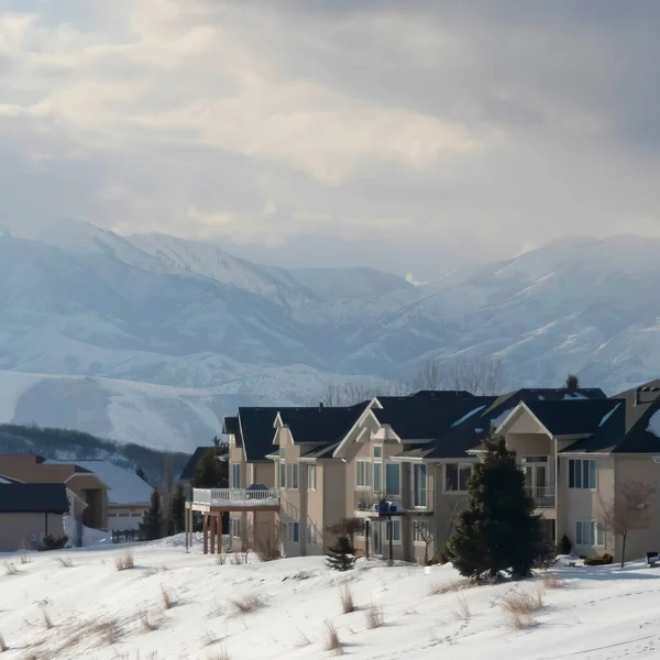 Cosecha cuadrada Casas en terreno nevado ovelooking Wasatch Mountain pico y cielo nublado oscuro — Foto de Stock