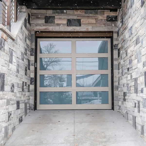 Neve quadrada caindo em casa com porta de garagem de painel de vidro e parede exterior de pedra — Fotografia de Stock
