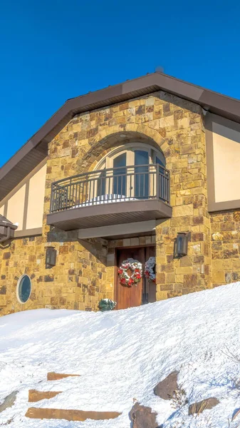 Marco vertical Casa de piedra con pequeño balcón sobre la puerta principal decorada con corona en invierno — Foto de Stock