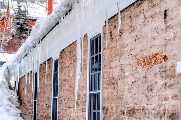 Cuadrado Sharp carámbanos puntiagudos contra las ventanas y la pared exterior de piedra del hogar en invierno — Foto de Stock