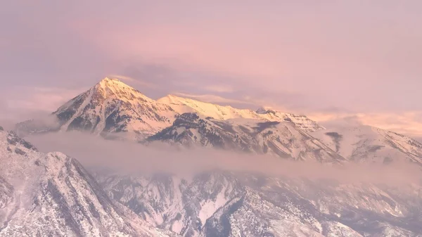 Панорама Снежная Васатч Гора и вершина холма, возвышающиеся над долиной Юты под облачным небом — стоковое фото