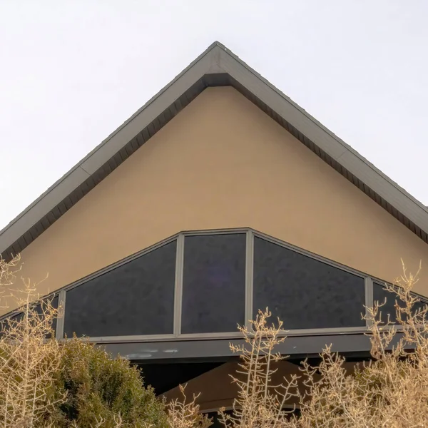 Квадратный дом с фронтальной двускатной крышей у входа, просматриваемый за деревьями и деревьями — стоковое фото