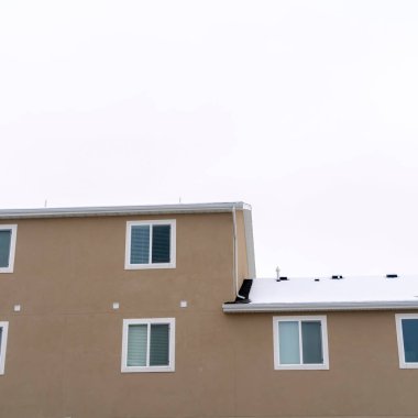 Duvarı karla kaplı, pencereleri kayan bir çatısı olan binanın kare dış görünümü