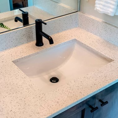 Tek atımlık lavabosu ve siyah musluğu olan kare banyo beyaz tezgahı.