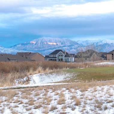 Kışın güneşte kavrulmuş dağlara karşı evleri olan karlı bir tepe.