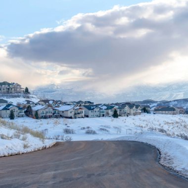 Bulutlu mavi gökyüzüne karşı evleri olan karlı dağdaki kare kıvrımlı yol
