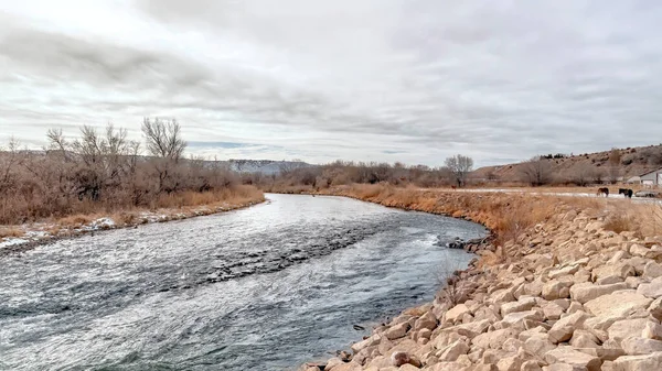 Panorama des cultures Rivière Glistening avec des rives herbeuses et rocheuses le long des maisons et des paysages de collines — Photo