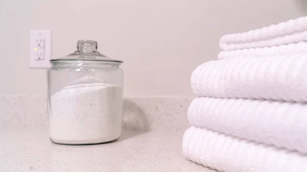 Panorama cultivo Plegable toallas blancas y frasco de vidrio con polvo blanco en la encimera del baño — Foto de Stock