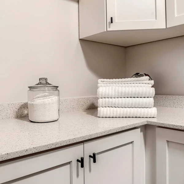 Square Countertop with jar of powder detergent and folded towels over wood cabinets
