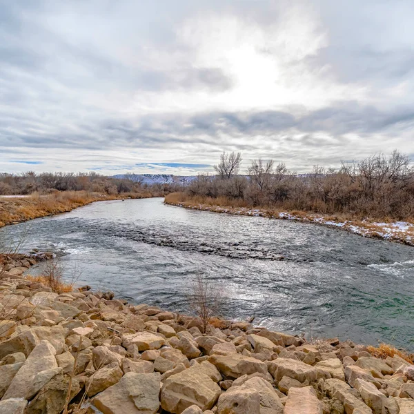 Square crop Glistening lake with dusting of snow on the rocky and grassy shore in winter — Stock Photo, Image