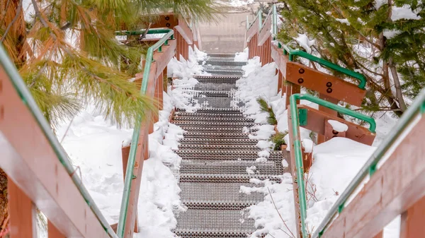 Panorama Mirando hacia abajo en la rejilla escaleras de metal con pasamanos en una colina nevada en invierno — Foto de Stock