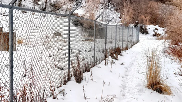 Panorama Chain link fence with barbed wires on snow covered hill slope viewed in winter