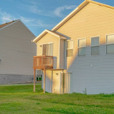 Kare Ekin Evi. Güneşli bir günde beyaz duvar kaplamalı çatı ve küçük balkon manzaralı.