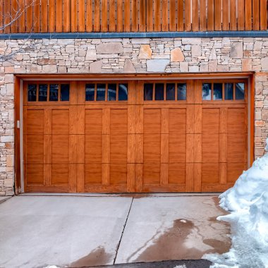 Kare mahsul, kahverengi ahşap cam pencereli garaj kapısı ev balkonunun altındaki taş duvara karşı.