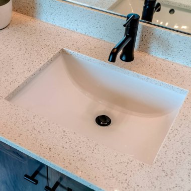 Kare hasat havzası lavabonun altında, beyaz tezgahta siyah musluk var.