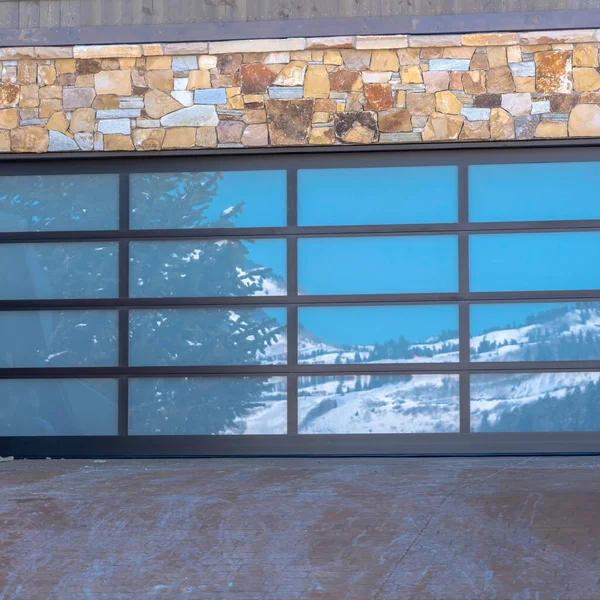 Kwadratowe drzwi garażowe ze szklanymi taflami odzwierciedlającymi śnieżny krajobraz wzgórza pod błękitnym niebem — Zdjęcie stockowe