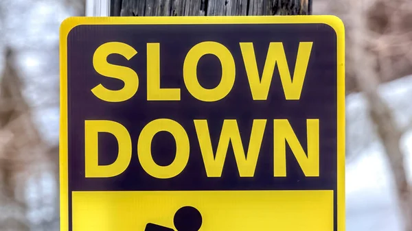 Panorama Black and yellow Slow Down Kids And Pets At Play sign against gray wooden pole — Stock Photo, Image