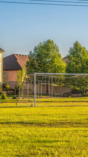 Cultivo vertical Fútbol objetivo en el vasto campo de hierba verde en frente de las casas vistas en un día soleado —  Fotos de Stock