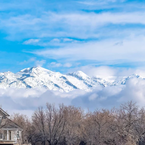 Cosecha cuadrada Picos de una magnífica montaña nevada sobre nubes bajas e hinchadas contra el cielo azul — Foto de Stock