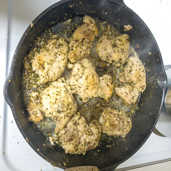 Square crop Slices of chicken meat with green herbs cooking on a hot cast iron skillet — Stock Photo, Image