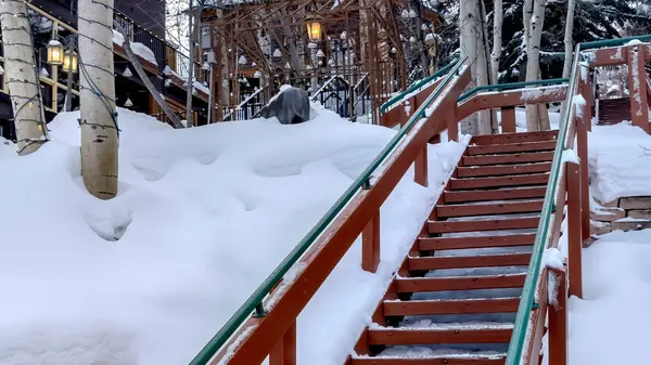 Panorama Outdoor stairs on snowy slope against buildings and trees on cloudy winter day