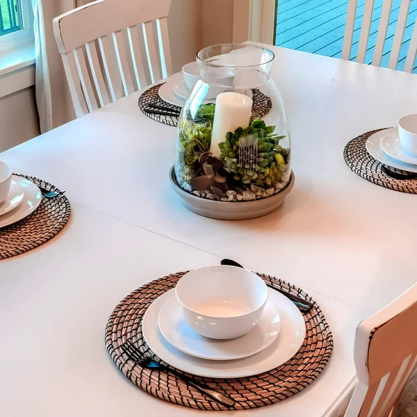 Square Dinner table setting with tableware on placemats arranged around a centerpiece