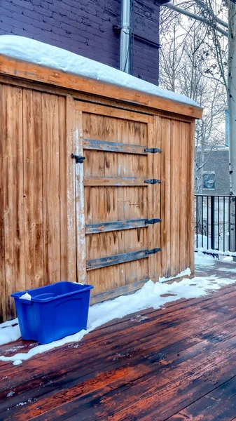 Vertical crop Wooden deck with snow shovel and bucket against storage cabinet and gray wall