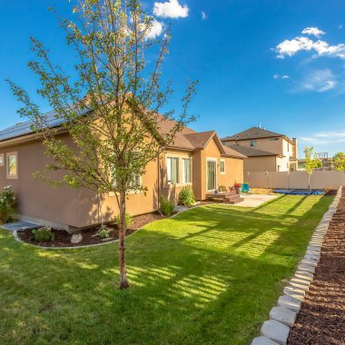 Kare çerçeveli, ağaçlarla çevrili, çimenli bir bahçe ve çit boyunca ekili bir yatak.