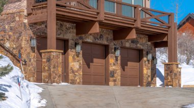 Güneşli bir kış gününde, karlı zeminin ortasında üç araba garajıyla Panorama Ev cephesi