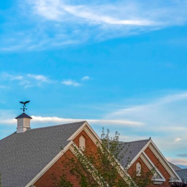 Kare mahsul Mavi gökyüzü ve ince bulutlar Gri gable çatı üzerinde havalandırma ve rüzgar gülü