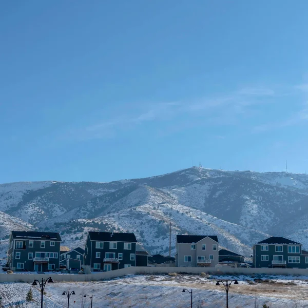 Rangée carrée de maisons contre les collines enneigées et le ciel bleu par une journée d'hiver sombre — Photo