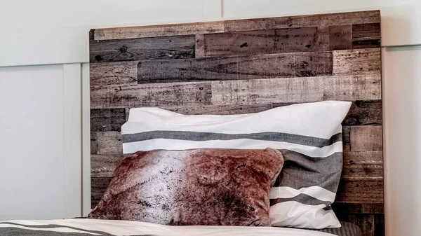 Panorama frame Bed with pillows against decorative wooden headboard against white panel wall