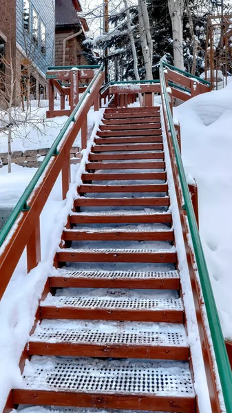 Vertical frame Outdoor stairs with grate metal treads and green handrail on snowy winter hill