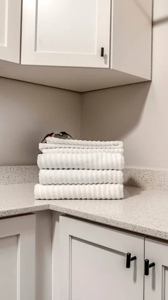 Vertical Countertop with jar of powder detergent and folded towels over wood cabinets