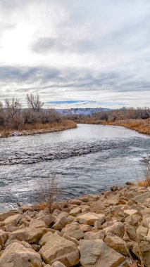 Dikey çerçeve, kışın kayalık ve çimenli sahilde kar tozuyla parıldayan göl.