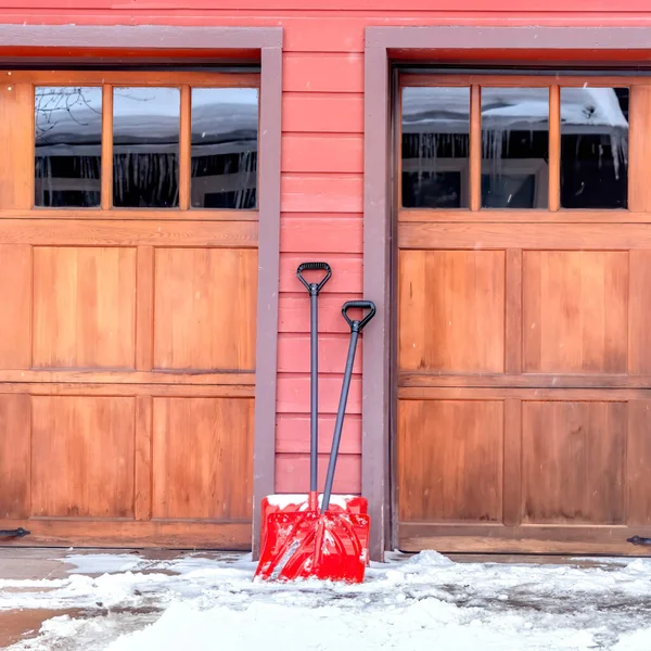 Palette rosse quadrate su vialetto innevato contro parete e porte garage in legno di casa — Foto Stock