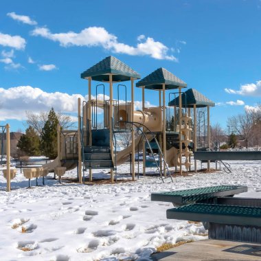 Kışın karlı zeminde ayak izleri olan çocuk parkı ve piknik masası.