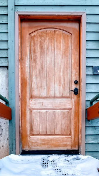 Снежная крытая лестница ведет к коричневой деревянной двери здания с голубой стеной — стоковое фото