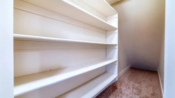 Panorama Small walk in closet with empty long cabinet shelves under slanted ceiling — Stock Image Panorama Small walk in closet with empty long cabinet shelves under slanted ceiling Stock Picture