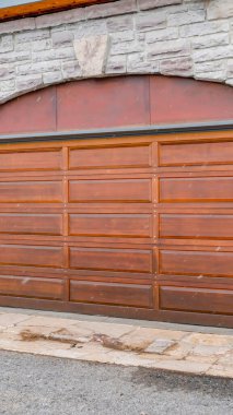 Dikey ekin kemerli kahverengi ahşap kapılı garaj kapısı taş tuğladan dış duvarlı.