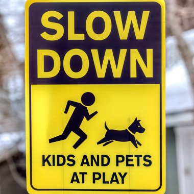 Square Black and yellow Slow Down Kids And Pets At Play sign against gray wooden pole clipart