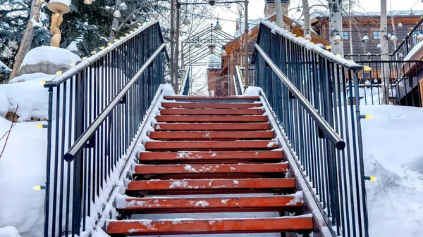 Panorama Stairs against snow covered slope with houses and trees under cloudy winter sky