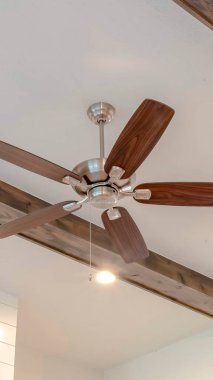 Evin oturma odasındaki dekoratif ahşap kirişler arasında ışıklı dikey tavan vantilatörü.